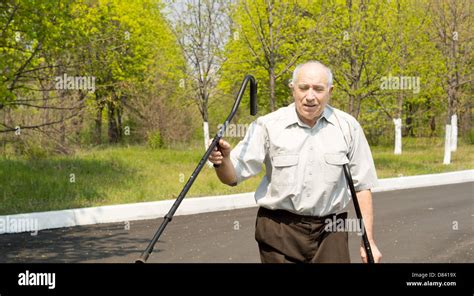 Senior Man Walking On Crutches Down A Rural Lane Waving One Crutch In