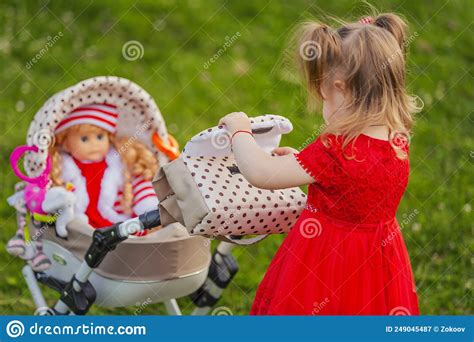 Girl Plays With Her Doll Who Is Sitting In A Stroller Stock Image