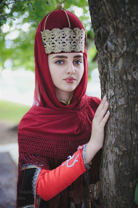 A Woman Wearing A Red Shawl And Headdress Standing Next To A Tree
