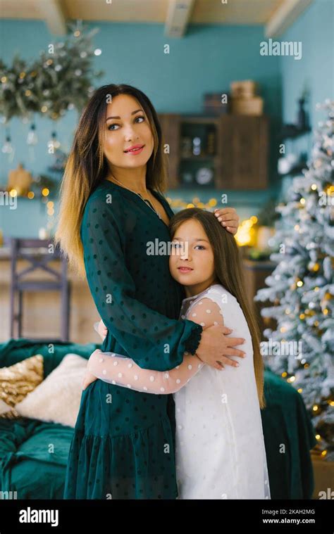 Mom And Daughter Hug Each Other Against The Background Of Christmas Decorations In The Living