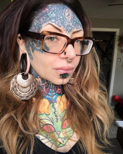 A Woman With Tattoos And Piercings On Her Face Is Wearing Eyeglasses While Looking At The Camera