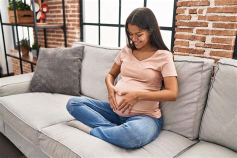 Joven Latina Embarazada Tocando El Vientre Sentada En El Sofá En Casa
