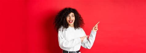 Free Photo Excited Pretty Girl With Curly Hair And Red Lips Looking And Pointing Fingers Left