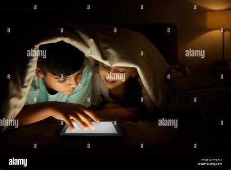 Brother And Sister Sharing Digital Tablet Under Blanket At Night Stock