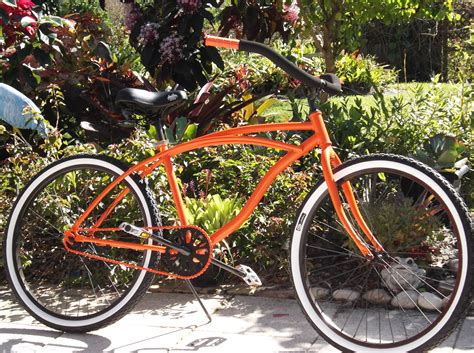 An Orange Bicycle Is Parked In Front Of Some Bushes And Flowers On The