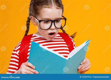 Astonished Schoolgirl Reading Textbook During Studies Stock Photo