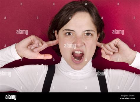 Young Woman Screams With Fingers In Her Ears And Red Background Stock