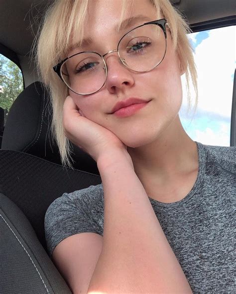 A Woman Wearing Glasses Sitting In The Back Seat Of A Car With Her Hand On Her Chin