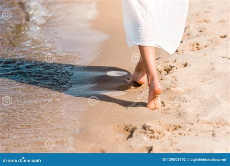 Partial View Of Barefoot Girl In White Dress Walking On Sandy Beach