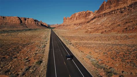 Drone Camera Follows Silver Car Moving Along Straight Desert Highway