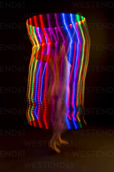 Blurred Rear View Of Nude Woman Standing In Tube Of Light Trails Stock