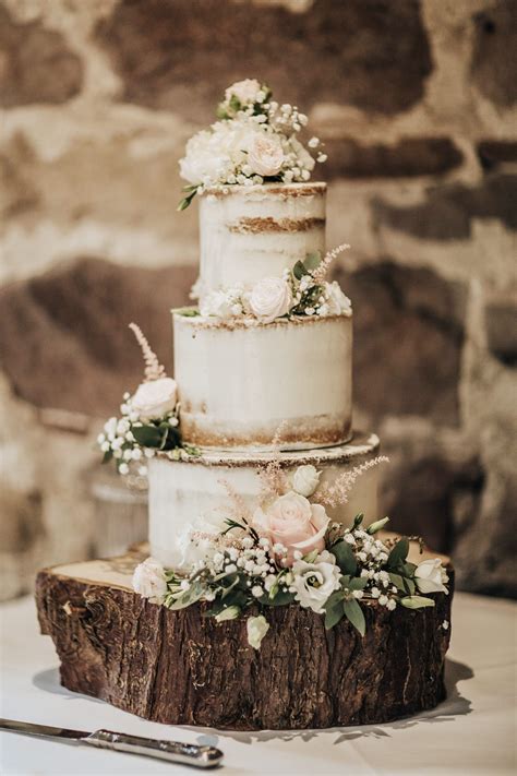 Semi Naked Wedding Cake With Pink Roses And Foliage Sitting On A Rustic Wooden Log Boho Wedding