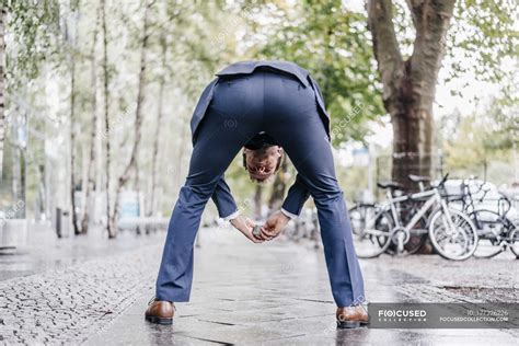 Back View Of Businessman Bending Over On Pavement Looking Through His