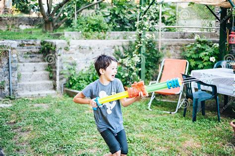Children Play In The Garden With Guns And Water Rifles On A Sunny