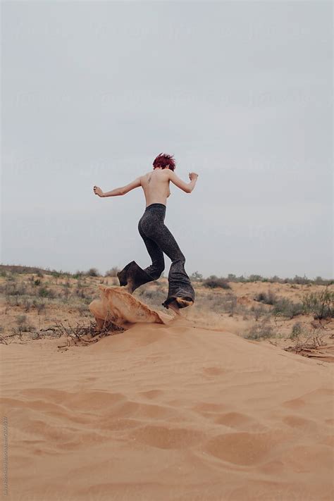 Unrecognizable Topless Redhead Girl Making Sand Splashes In Desert Del Colaborador De Stocksy