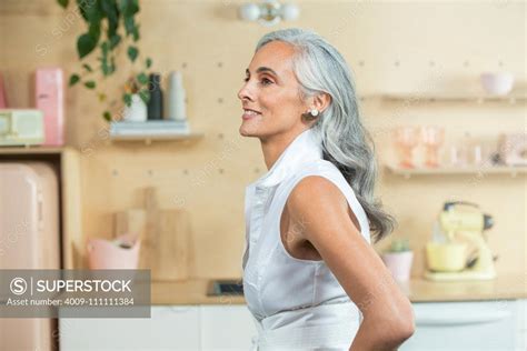 Standing In A Modern Kitchen A Youthful Middle Aged Woman With Gray Hair Looks Off Camera