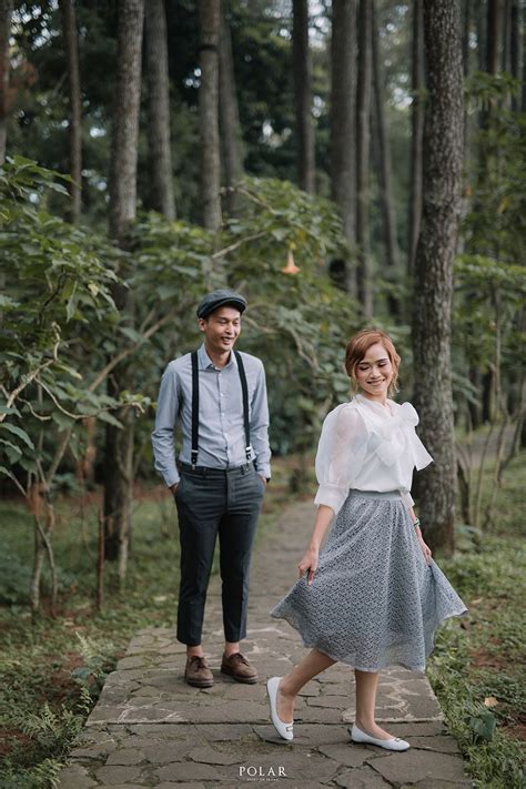 A Man And Woman Walking Down A Path In The Woods With One Holding His Hand