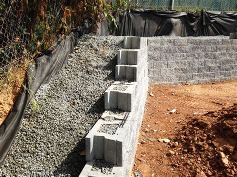 A cinder block retaining wall needs a poured concrete or gravel foundation, footings, and grout filling and rebar for support. permeable-concrete-retaining-wall | CornerStone Wall Solutions