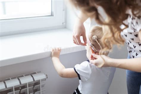 Mother Helps Her Deaf Baby Daughter Putting Hearing Aid In Little Girl