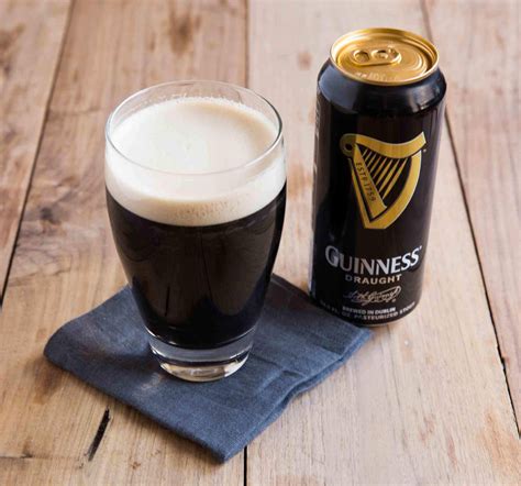 A Glass Of Beer Next To A Can Of Guinness On A Wooden Table With A Cloth
