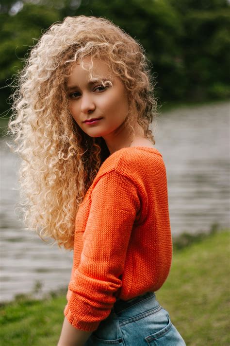 curly haired blond woman in orange shirt blick auf ihre seite · kostenloses stock foto