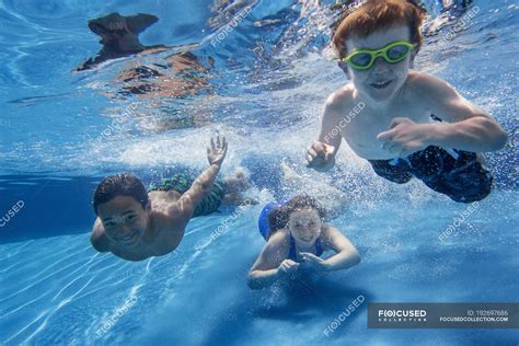 Three Children Swimming Underwater And Smiling In Camera — Mixed Race