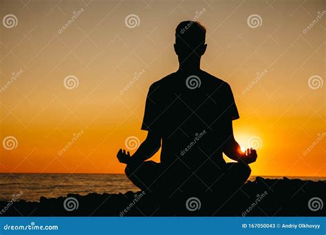 Silhouette Of A Man In Meditation Pose On Beach On Sea Background And