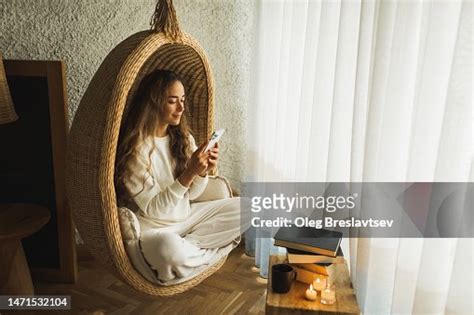 Young Woman Relaxing In Hanging Wicker Chair With Mobile Phone Wasting Time And Procrastination