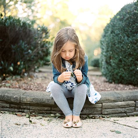 Cute Young Girl Sitting Outside Playing With A Leaf By Stocksy