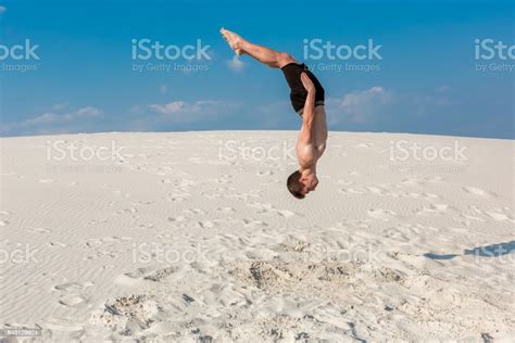 Portrait Of Young Parkour Man Doing Flip Or Somersault On The Sand