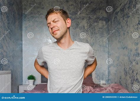 Young Caucasian Man Suffering From Back Pain While Sitting On A Bed At