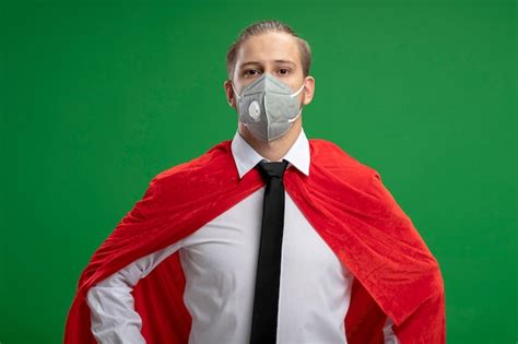 의료 마스크를 착용하고 녹색 배경에 고립 된 카메라를보고 넥타이 자신감 젊은 슈퍼 히어로 남자 무료 사진