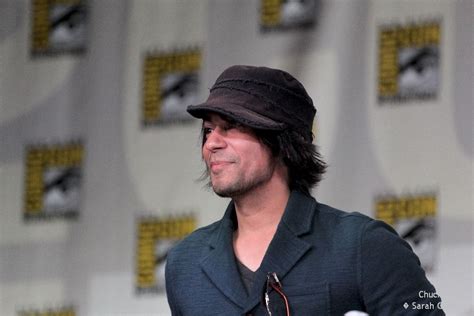 A Man Wearing A Hat And Tie Standing In Front Of A Wall With Microphones