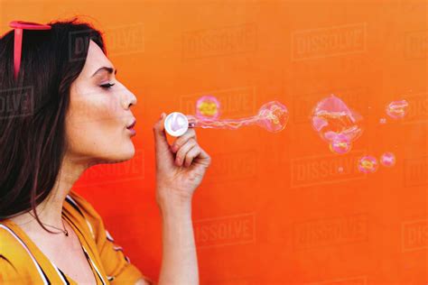 Side View Shot Of Young Beautiful Female Blowing Soap Bubbles Against