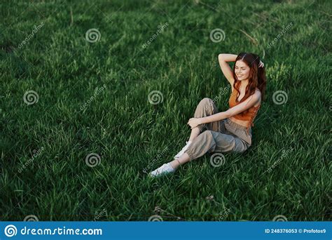 A Woman Enjoying The Outdoors Sitting In The Park On The Green Grass In Her Casual Clothes Lit