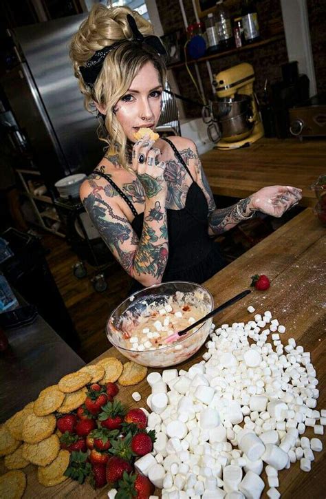A Woman With Tattoos Standing In Front Of A Table Filled With Marshmallows