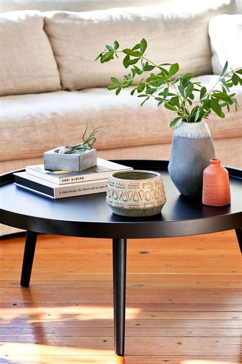 A Coffee Table With Two Vases And Books On It In Front Of A Couch