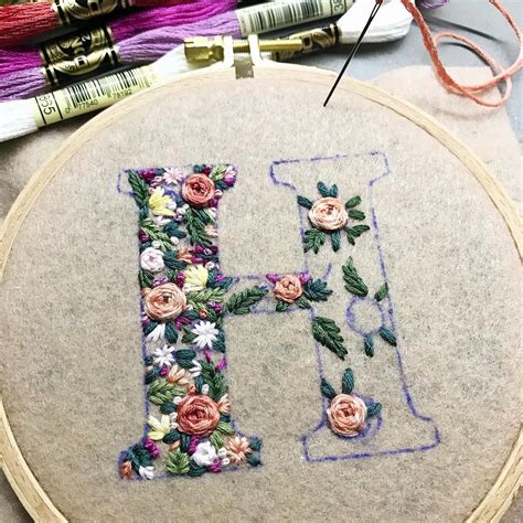 The Letter H Is Made Up Of Flowers And Leaves On A Gray Surface Next To Some Thread