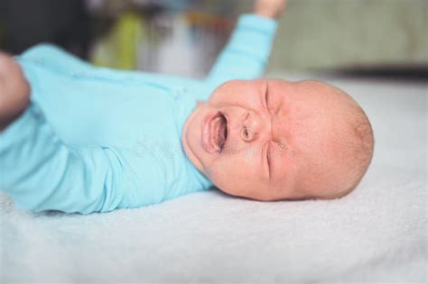 Cute Emotional Crying Newborn Infant Boy In Blue Jumpsuit Laying On Bed