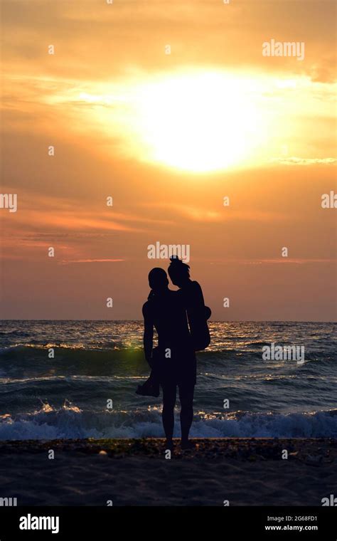 Silhouette Of Man Carrying Woman In His Arms On The Beach At Sunset