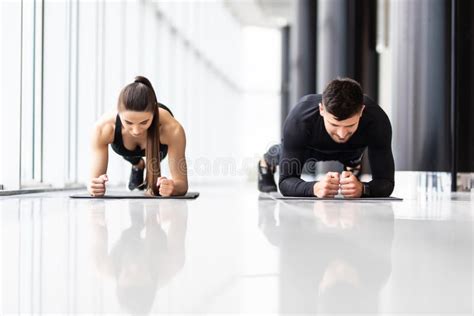 Portrait Of A Muscular Couple Doing Planking Exercises At Gym Stock