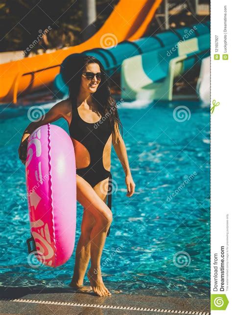 Mujer Que Lleva A Cabo El Anillo Inflable Rosado Cerca De Piscina Con Las Diapositivas Imagen De