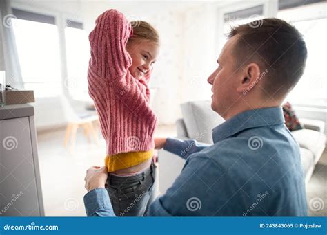father helping his little daughter with down syndrome to wear trousers at home stock image