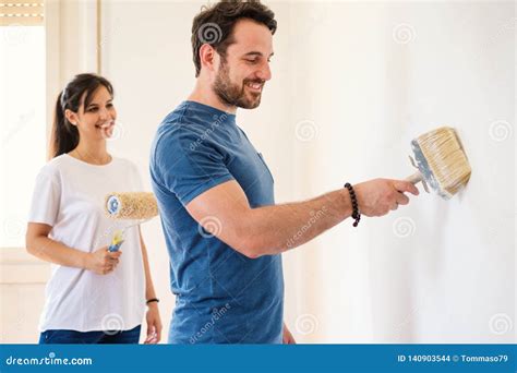 Young Couple Painting Walls In Their New House Do It Yourself Concept