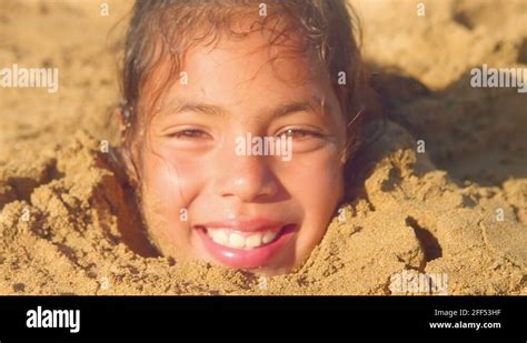 A Young Girl Is Buried In Sand Up To Her Neck Smiling Close Up Stock