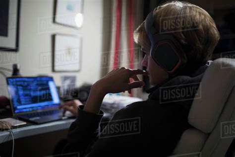 Teenage Boy With Headphones Using Computer In Dark Bedroom Stock