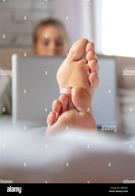 Focus On The Feet In The Foreground A Teenage Girl Is Lying On A Bed
