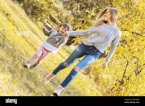 beautiful woman holding hand of her little daughter and smiling while running together in autumn