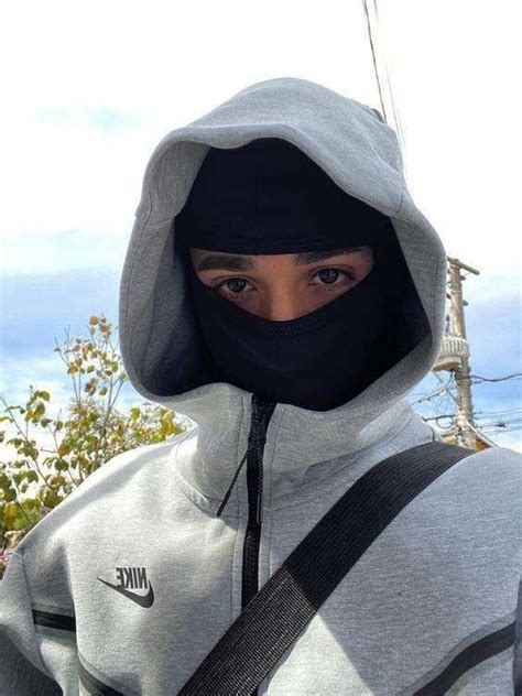 a person wearing a hoodie and carrying a bag in front of the camera with their face covered by a