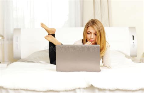 jovem mulher que senta se na cama em casa e que usa o laptop imagem de stock imagem de café